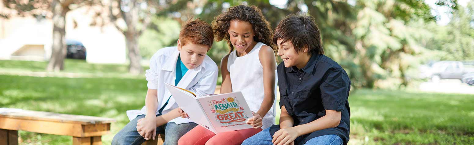 three children outside on a bench looking at a yearbook